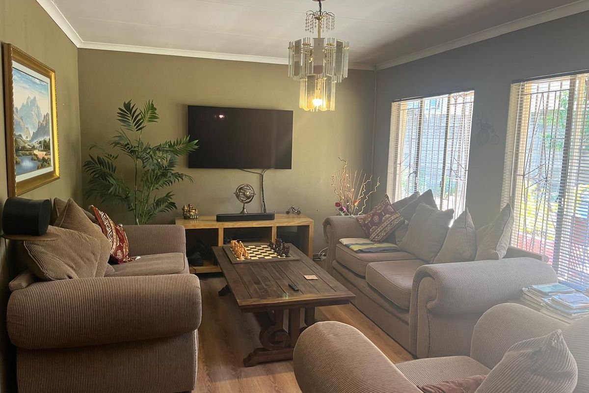 A comfortable living room featuring laminate flooring, decorative cove cornicing, and a classic crystal chandelier, with security bars fitted to the windows.