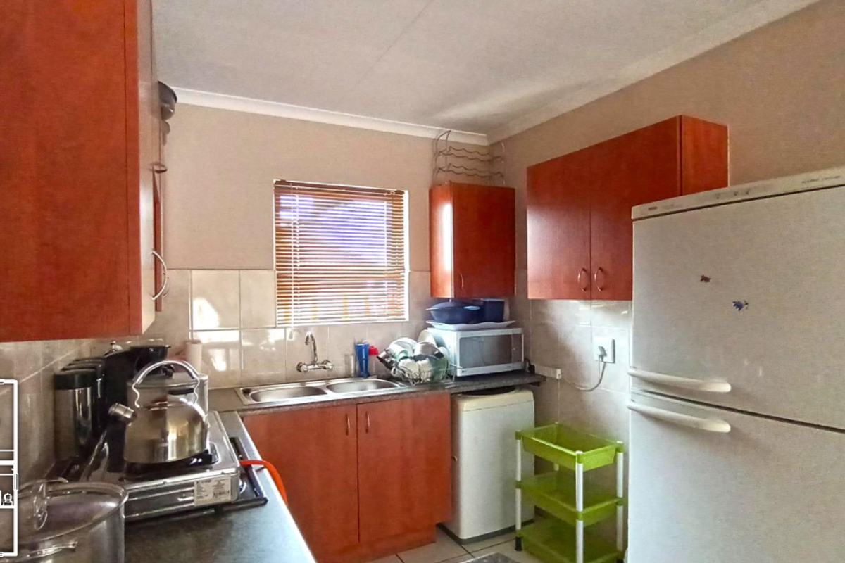 A functional kitchen featuring wood-tone cabinetry, a double bowl sink, tiled splashbacks, and a built-in hob, providing a practical workspace for daily cooking.