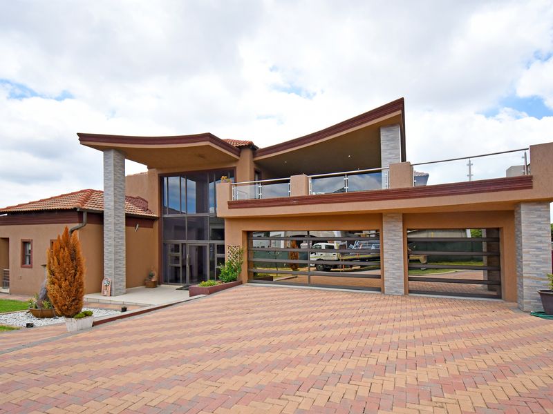 Modern double-story residence featuring a paved driveway, double garage, stone-clad pillars, and an expansive glass entrance with an upper-level balcony.