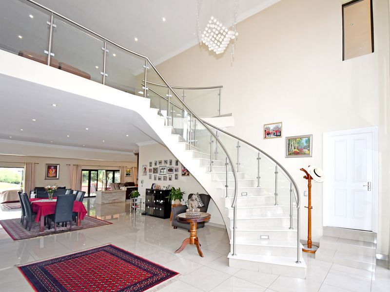 Spacious open-plan living area featuring a striking curved staircase with glass balustrades, high ceilings, and polished porcelain floor tiles.