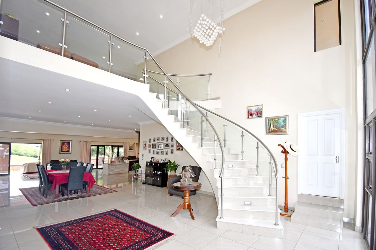 Spacious open-plan living area featuring a striking curved staircase with glass balustrades, high ceilings, and polished porcelain floor tiles.