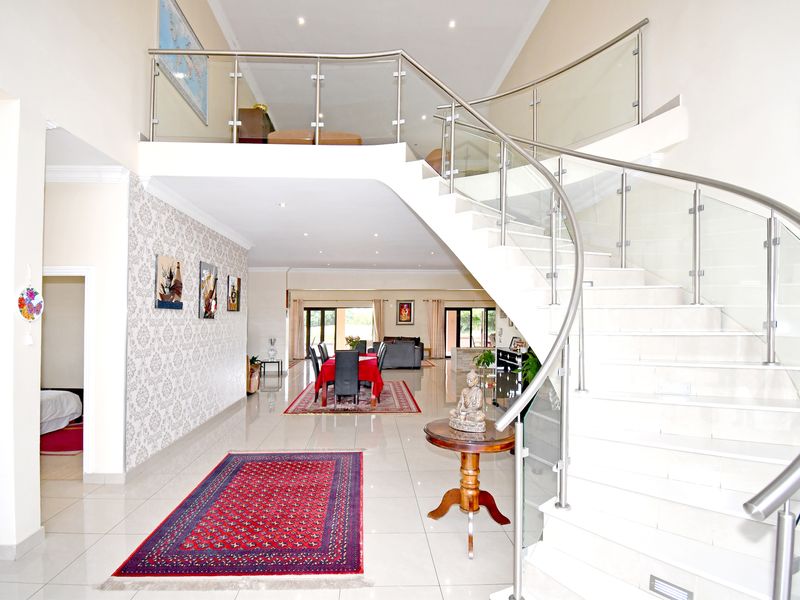 Spacious open-plan living area featuring a striking curved staircase with glass balustrades, high ceilings, and polished tiled flooring throughout.