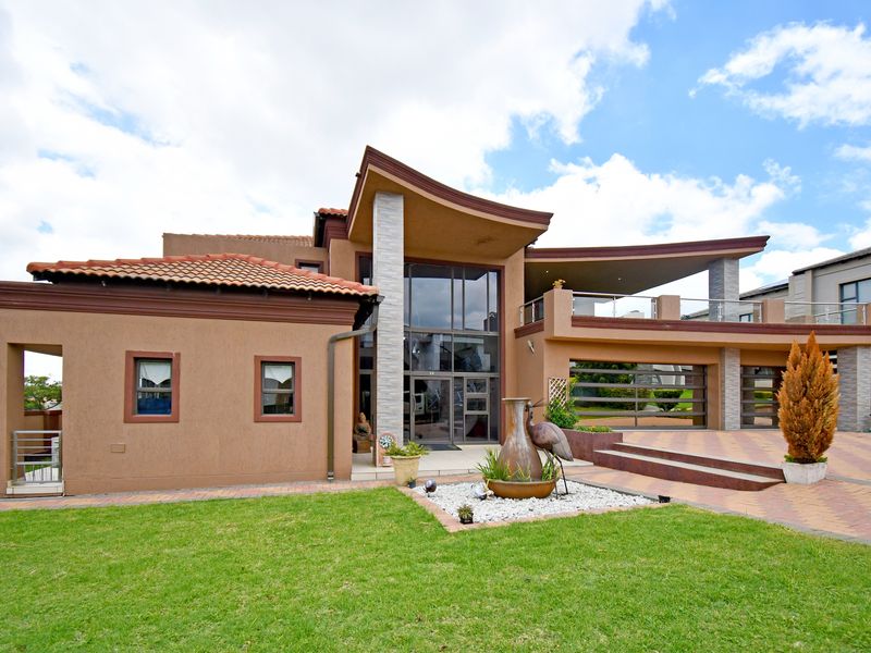 Modern architectural house exterior featuring a striking curved roofline, large glass facade, paved driveway, and an elevated balcony area.