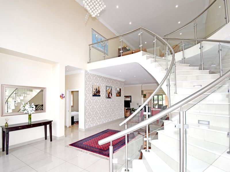 Grand entrance hall featuring a striking curved staircase with glass balustrades, high double-volume ceilings, and polished tiled flooring.