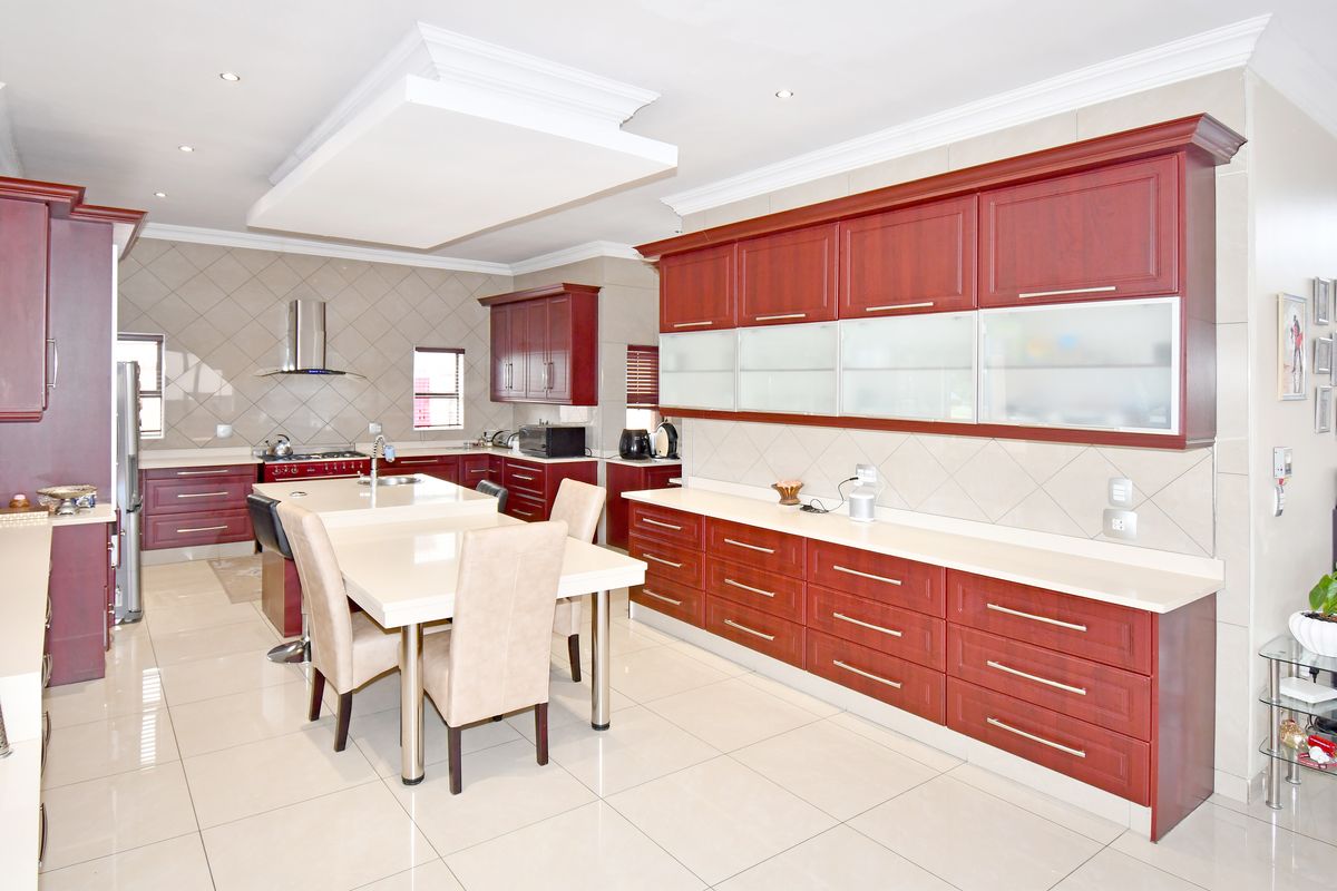 Spacious modern kitchen featuring extensive cherry-wood cabinetry, a central island with integrated dining, stone countertops, and high-quality tiled finishes throughout.