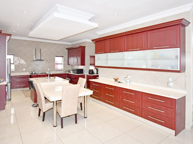 Spacious modern kitchen featuring extensive cherry-wood cabinetry, a central island with integrated dining, stone countertops, and high-quality tiled finishes throughout.