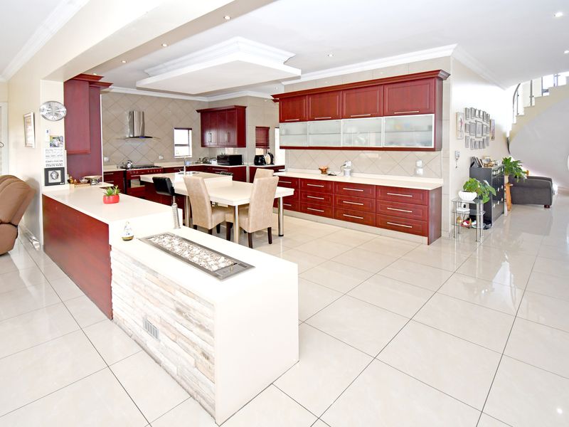Spacious open-plan kitchen featuring cherry wood cabinetry, stone countertops, and integrated appliances, seamlessly flowing into the living area with tiled flooring throughout.