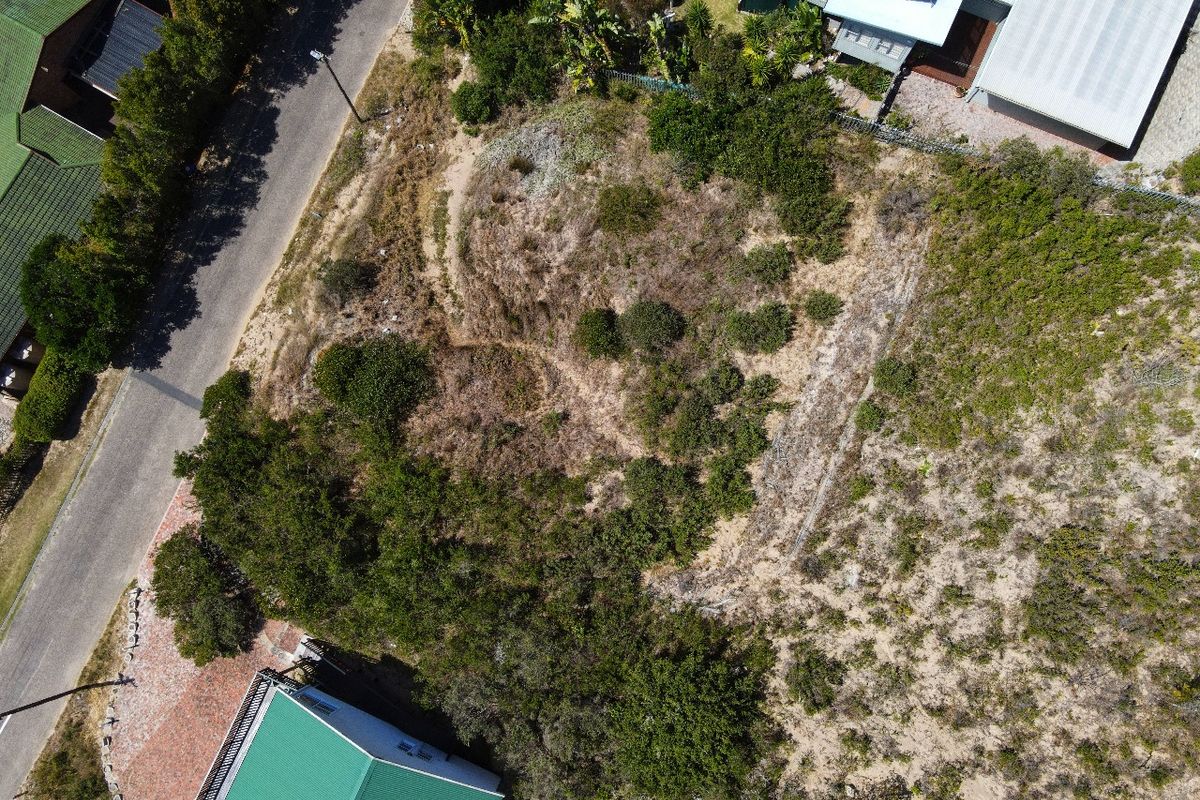 An aerial view of a vacant residential plot featuring natural vegetation and direct access to the adjacent paved road.
