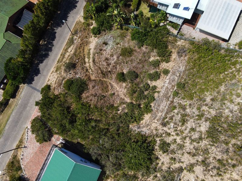 An aerial view of a vacant residential plot featuring natural vegetation and direct access to the adjacent paved road.
