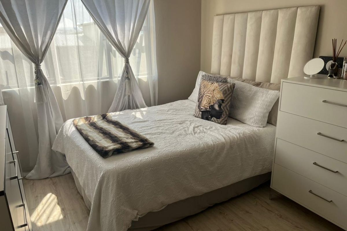 A well-maintained bedroom featuring light-toned laminate flooring and large windows with curtain rails, offering a bright and comfortable living space.