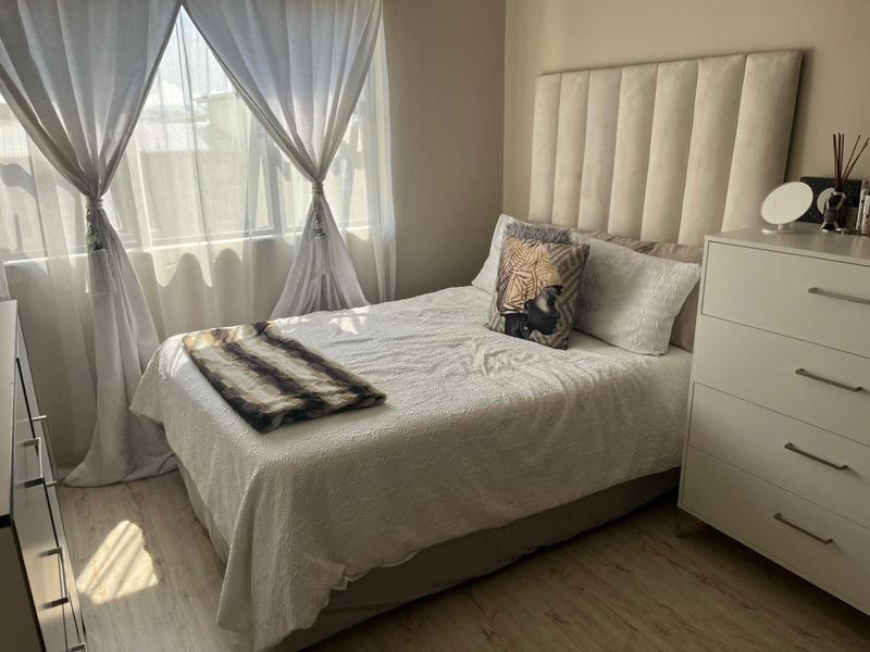 A well-maintained bedroom featuring light-toned laminate flooring and large windows with curtain rails, offering a bright and comfortable living space.