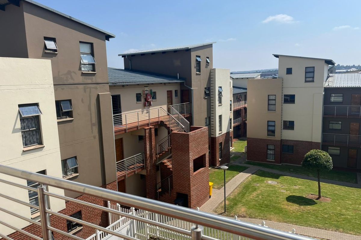 View of the apartment complex exterior, featuring brick and rendered facades, external staircases, metal balustrades, and a well-maintained communal garden area.