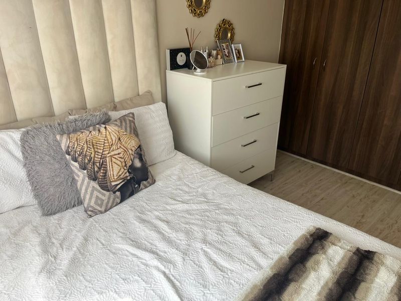 A well-maintained bedroom featuring a neutral upholstered headboard, wood-finish built-in wardrobes, and light-toned laminate flooring.