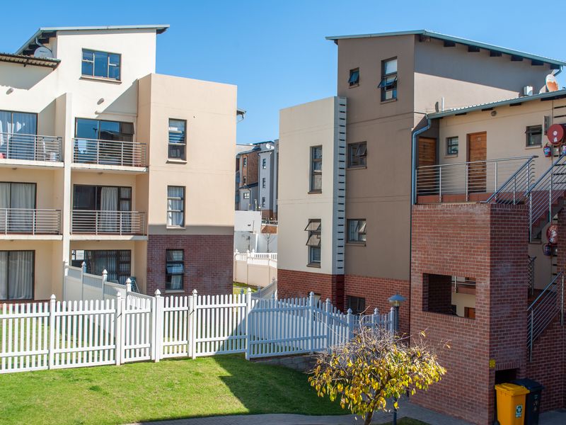 Exterior view of modern apartment blocks featuring brick and rendered facades, private balconies with metal railings, and a landscaped communal garden area.