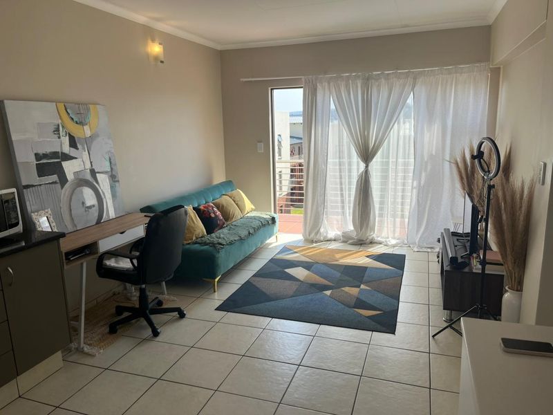 A bright living room featuring tiled flooring and a sliding glass door that provides access to an outdoor balcony area.