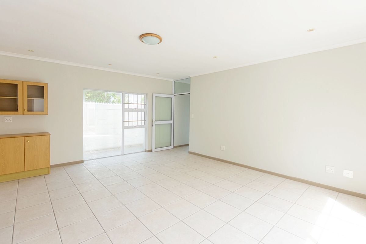 A bright, empty living area featuring neutral tiled flooring, built-in wooden cabinetry, and direct access to an outdoor space through a glass sliding door.