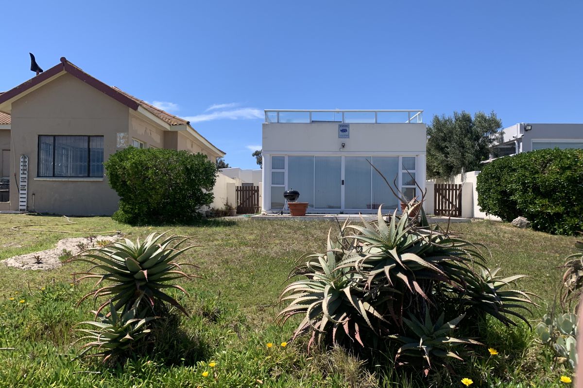 Rear view of the property featuring a garden, paved patio area, and a modern structure with sliding glass doors and a rooftop terrace.