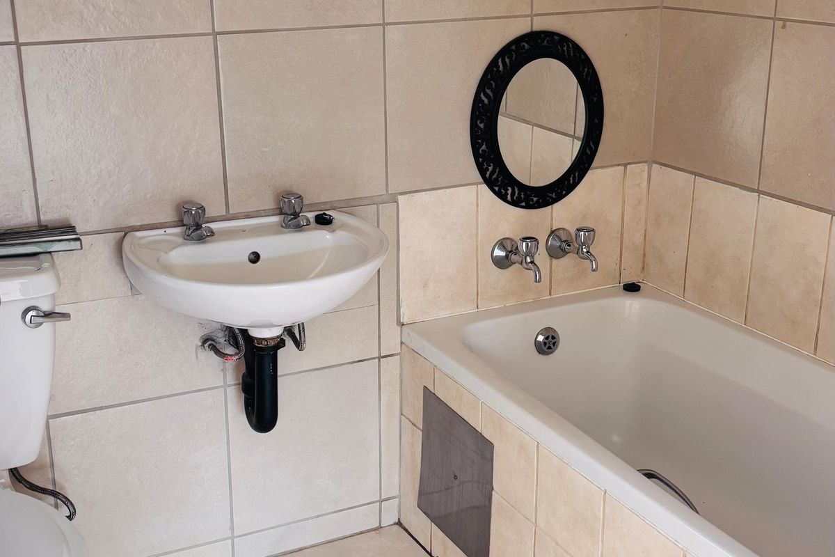 A functional bathroom featuring a built-in bathtub, wall-mounted basin, and neutral ceramic tiling throughout.