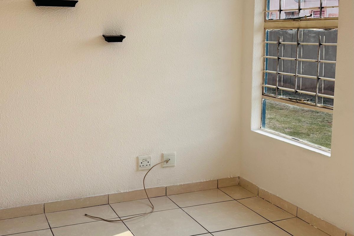 A bright, empty bedroom featuring neutral tiled flooring, security bars on the window, and clean white walls.