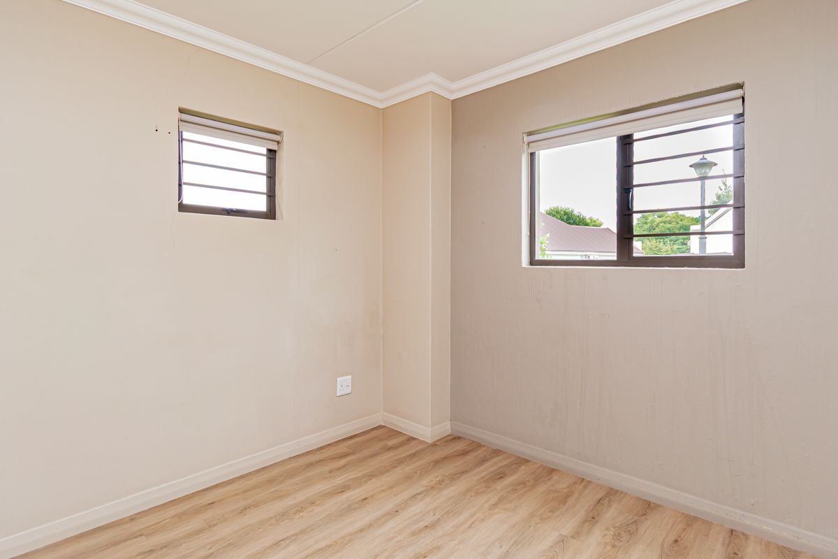 An empty bedroom featuring laminate flooring, neutral wall tones, and windows fitted with security bars.