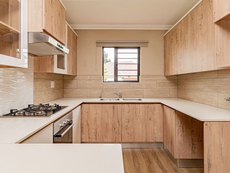 Modern kitchen featuring light wood-grain cabinetry, stone countertops, a gas hob, built-in oven, and a double sink with tiled backsplash.