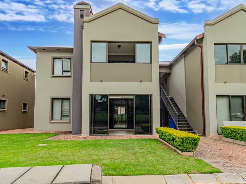 Rear view of the apartment building featuring a private lawn, paved walkway, external staircase, and sliding glass doors leading into the living area.