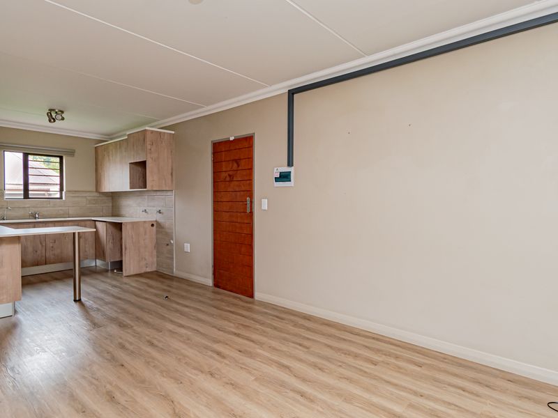An open-plan living and kitchen area featuring light wood-look laminate flooring, modern cabinetry, and a tiled backsplash, presenting a clean, blank canvas for styling.