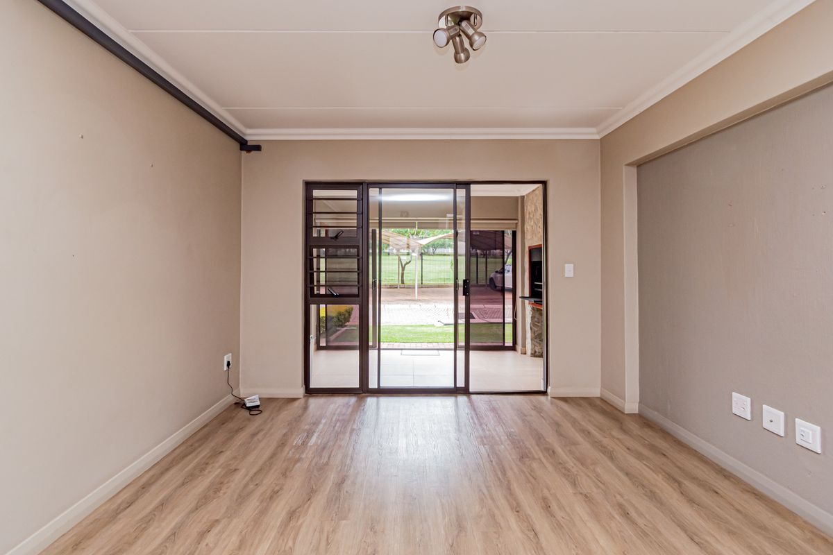 An empty, well-maintained living room featuring laminate flooring, neutral walls, and a sliding glass door providing access to an outdoor patio area.