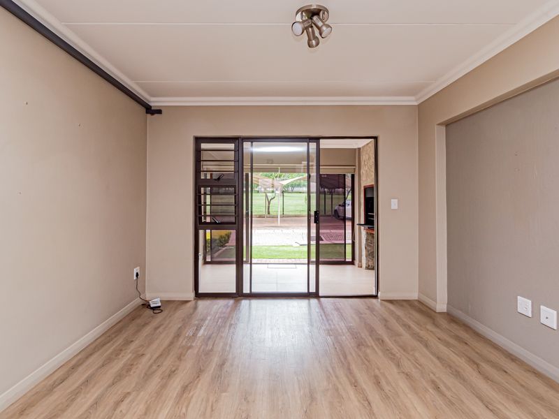 An empty, well-maintained living room featuring laminate flooring, neutral walls, and a sliding glass door providing access to an outdoor patio area.