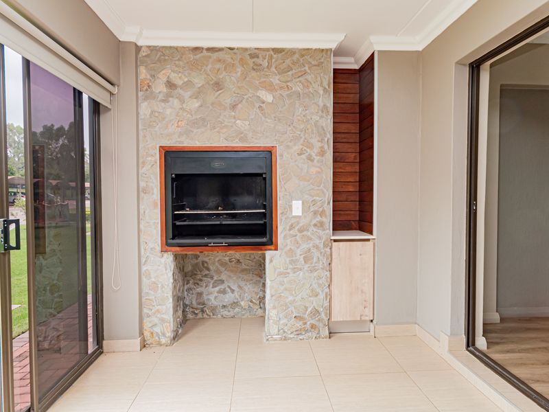 Covered patio area featuring a built-in stone-clad braai, timber accents, tiled flooring, and large sliding glass doors providing access to the garden.
