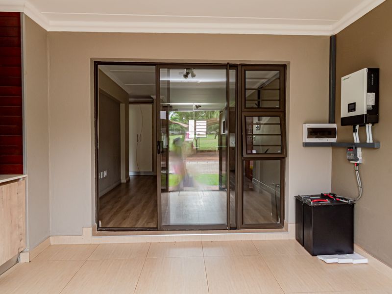A covered patio area featuring tiled flooring, stone accent wall, and a modern solar power installation with inverter and battery storage.