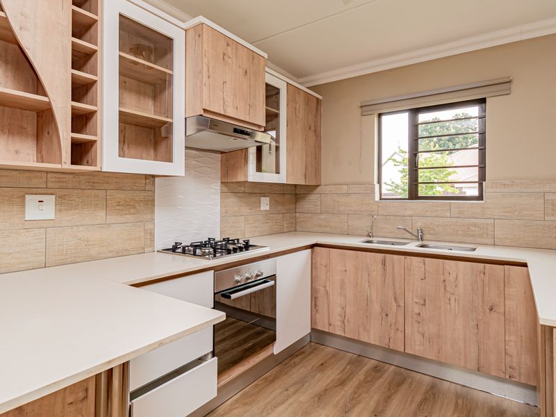 Modern kitchen featuring light wood-grain cabinetry, stone-look countertops, a gas hob, built-in oven, and a double sink with a tiled backsplash.