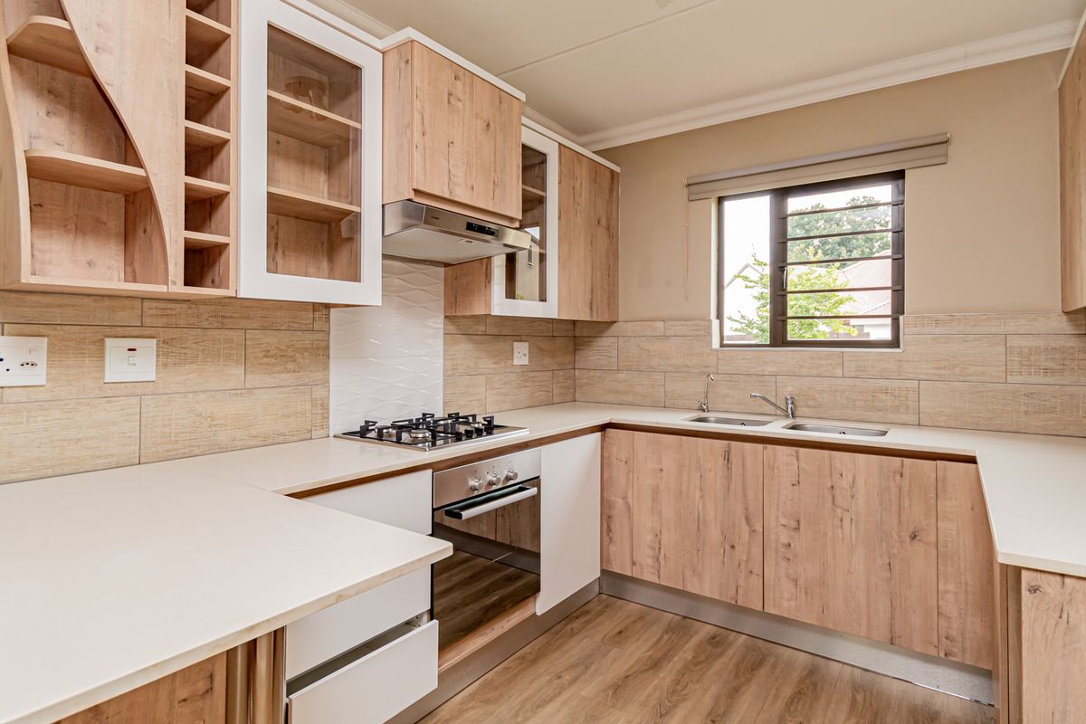 Modern kitchen featuring light wood-grain cabinetry, stone-look countertops, a gas hob, built-in oven, and a double sink with a tiled backsplash.