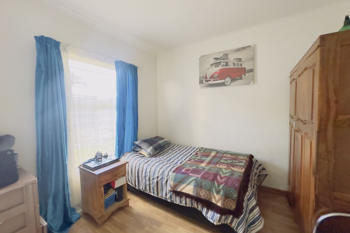 A standard bedroom featuring laminate flooring and a window with curtains, providing a functional space for rest.