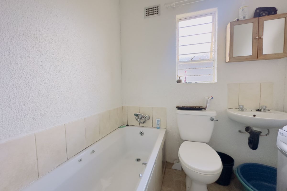 A functional bathroom featuring a standard bathtub, toilet, and wall-mounted basin with louvered window ventilation and tiled splashback finishes.