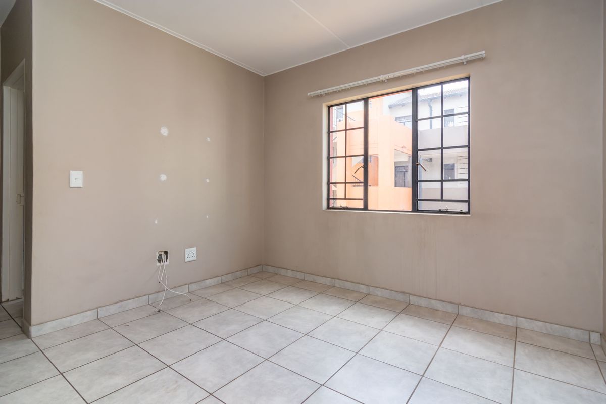An empty bedroom featuring tiled flooring, a window with security bars, and visible wall surface imperfections requiring minor repairs.