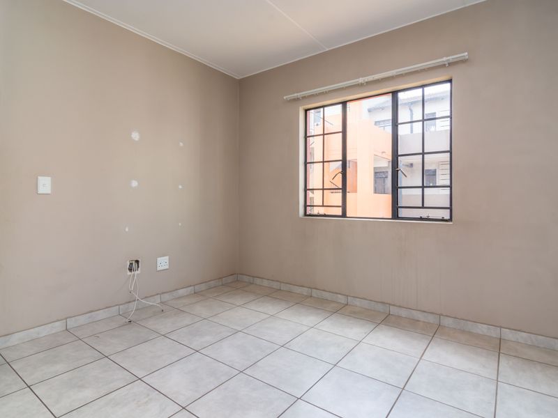 An empty bedroom featuring tiled flooring, a window with security bars, and visible wall surface imperfections requiring minor repairs.