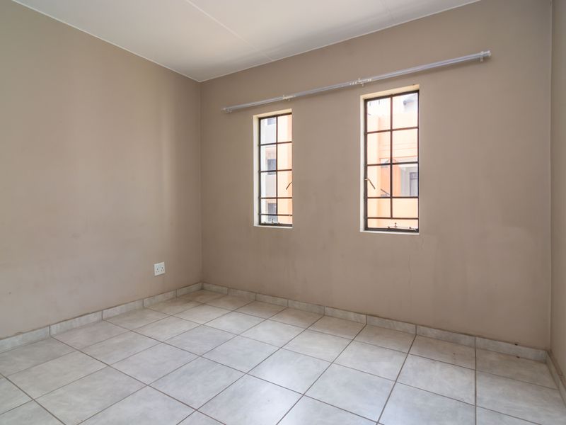 An empty bedroom featuring neutral wall paint, tiled flooring, and two windows fitted with security burglar bars.