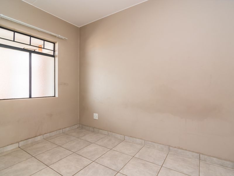 An empty bedroom featuring neutral tiled flooring and a window with security bars, requiring minor cosmetic attention to the walls.