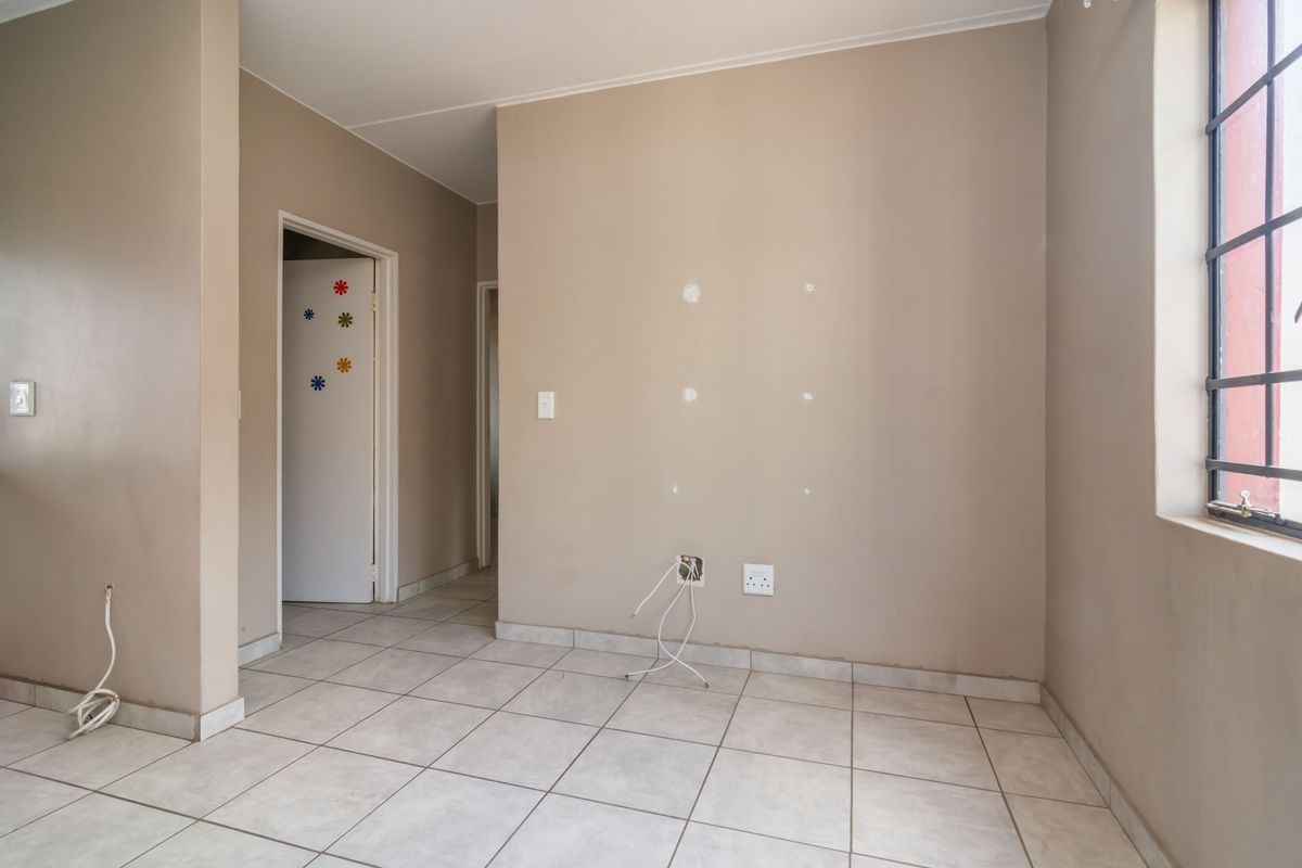 An empty living area featuring tiled flooring, security bars on the window, and visible wall damage requiring minor repairs and cosmetic updates.