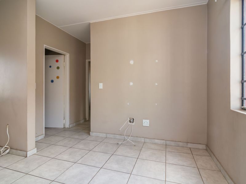 An empty living area featuring tiled flooring, security bars on the window, and visible wall damage requiring minor repairs and cosmetic updates.