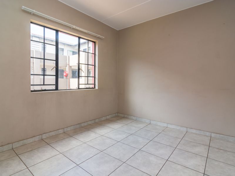 An empty bedroom featuring neutral wall tones, tiled flooring, and a window with security bars, offering a blank canvas for personalization.