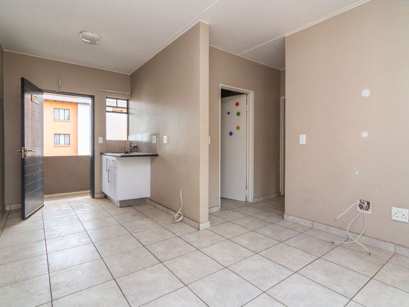 An open-plan living area featuring tiled flooring, a compact kitchen sink unit, and direct access to an exterior balcony.