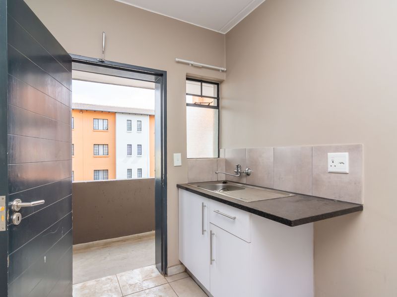 A compact scullery area featuring built-in cabinetry, a stainless steel sink, tiled splashback, and direct access to an outdoor balcony.
