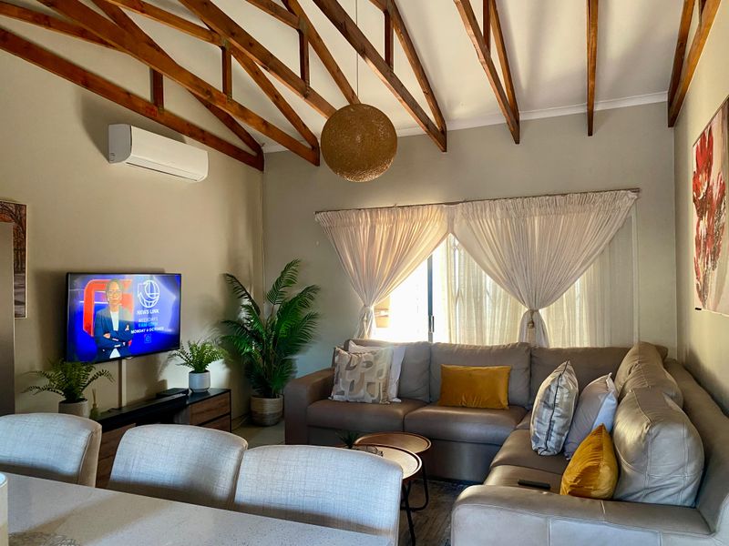 Open-plan living area featuring high vaulted ceilings with exposed timber trusses, tiled flooring, and a wall-mounted air conditioning unit.