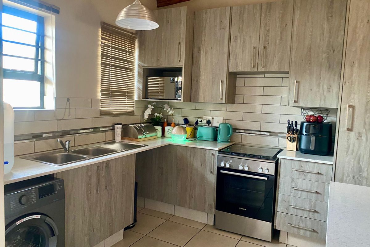 A functional kitchen featuring wood-look cabinetry, a tiled backsplash, double sink, and a stainless steel freestanding oven with integrated microwave.