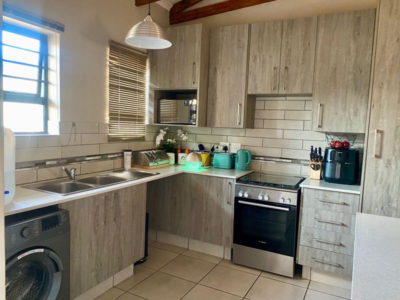 A functional kitchen featuring wood-look cabinetry, a tiled backsplash, double sink, and a stainless steel freestanding oven with integrated microwave.