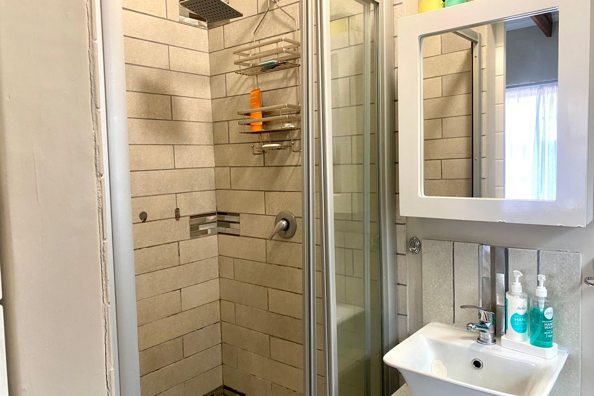 Compact bathroom featuring a tiled shower enclosure with a rain shower head, a vessel sink, and a wall-mounted vanity mirror.