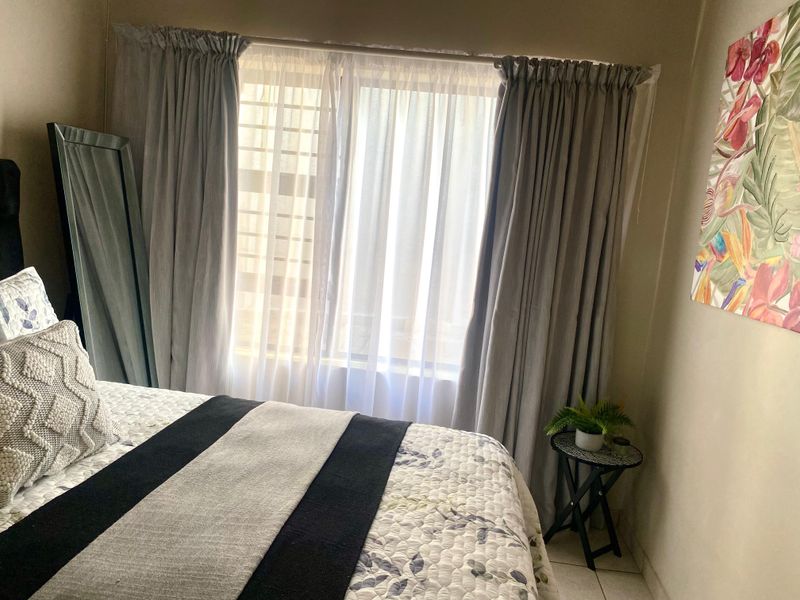 A cozy bedroom featuring tiled flooring and a window fitted with security bars, allowing for natural light.