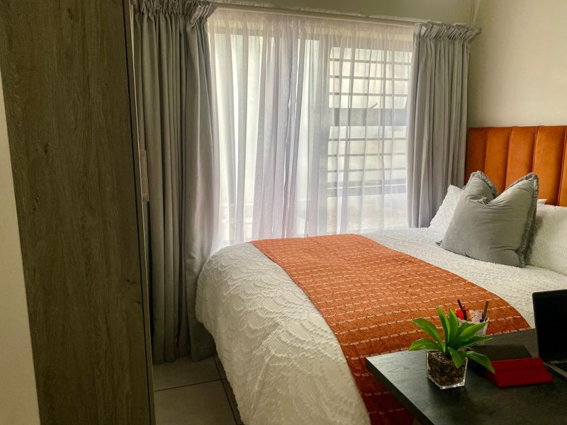 A cozy bedroom featuring tiled flooring, a built-in wardrobe, and a window fitted with security bars, providing natural light and functional storage.